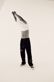 male model in white top and black velour tracksuit bottoms removing his tshirt in black and white