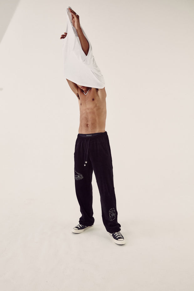 male model in white top and black velour tracksuit bottoms removing his tshirt